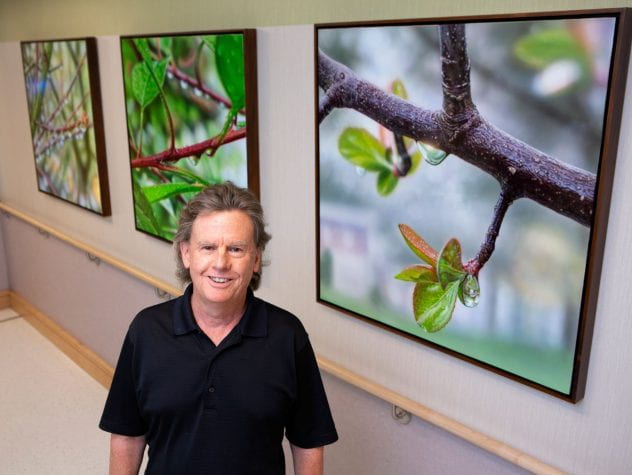 Bruce Evans standing next to his 3 pieces of artwork that are hanging in the HVI Corridor