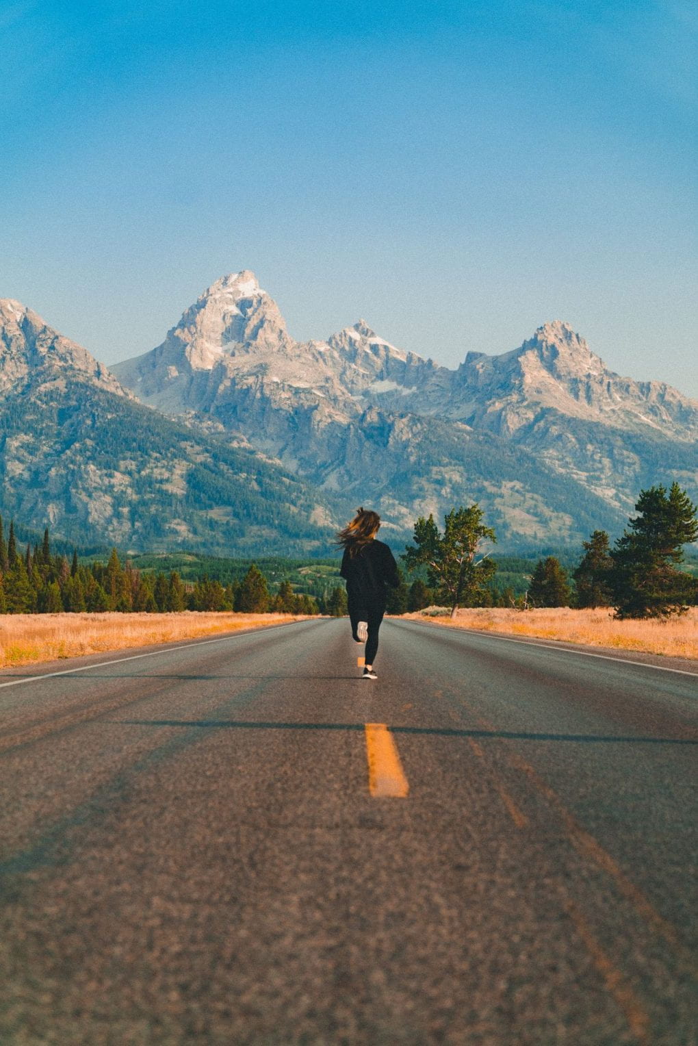 Woman running down the middle of the road with mountains in the distance