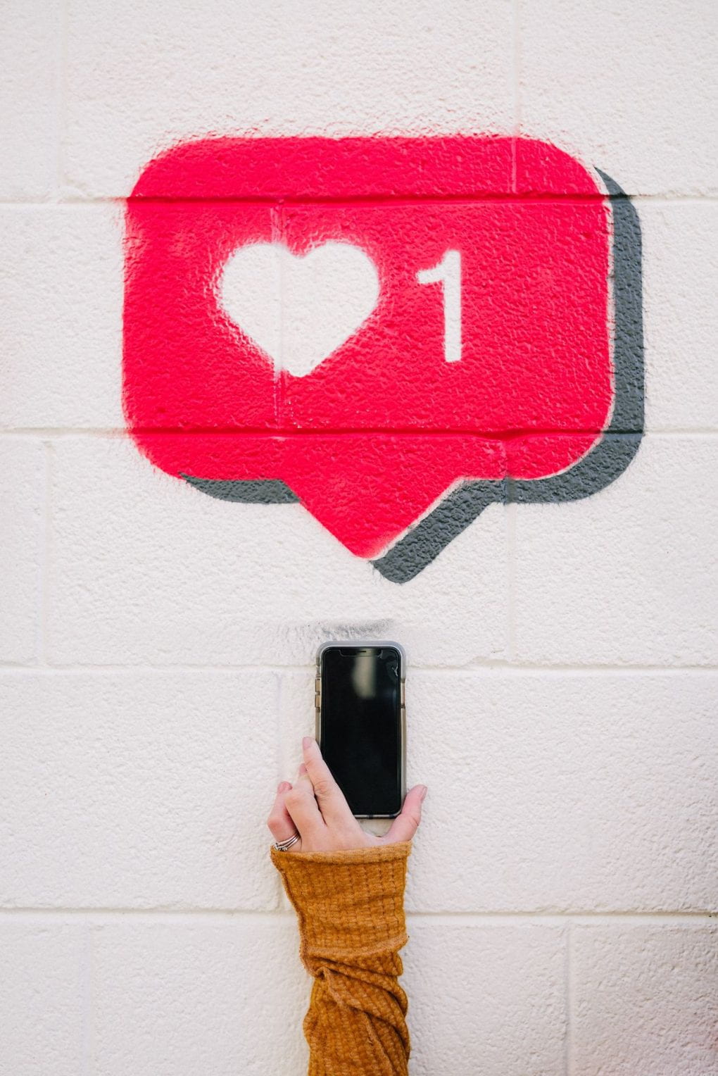 graffiti art of red and white social media love alert above smartphone being held by hand
