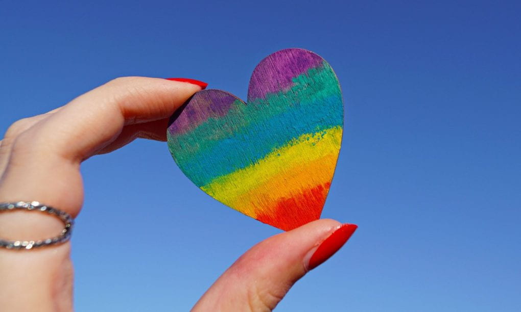 Close up photograph of person holding rainbow colored heart