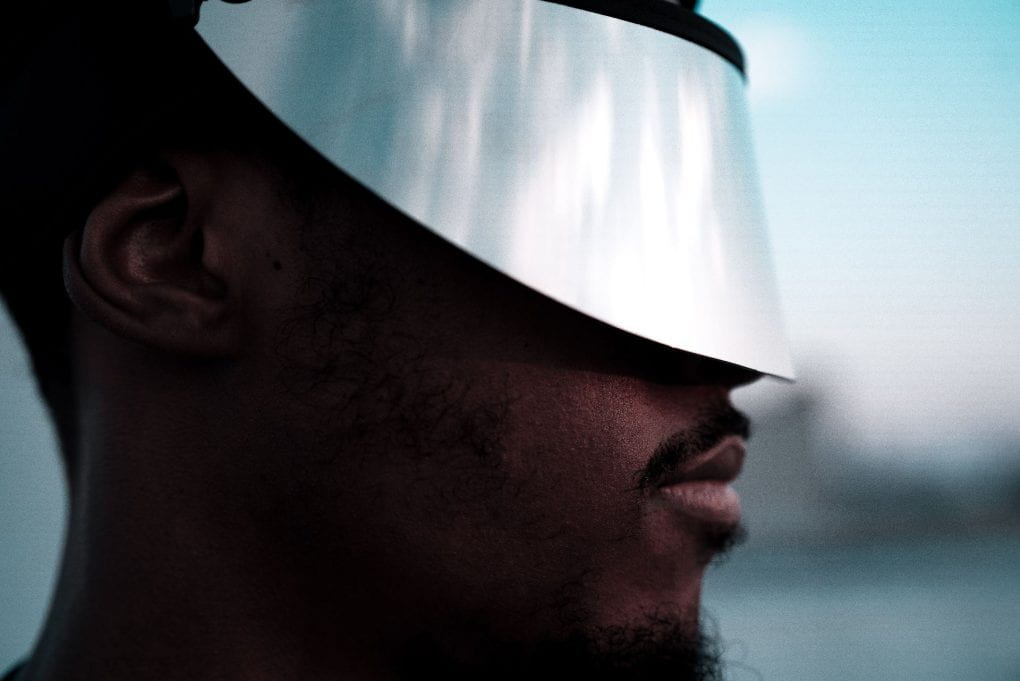 close-up portrait of a black man wearing a reflective silver visor over his eyes