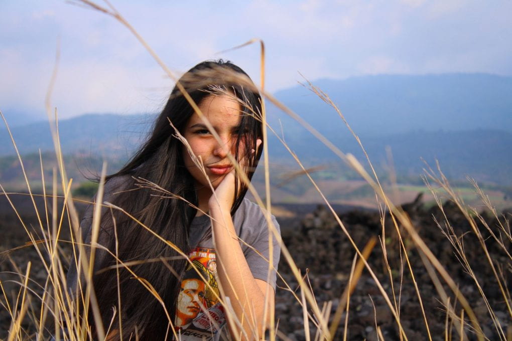 Woman sitting in grass field in front of mountains in background
