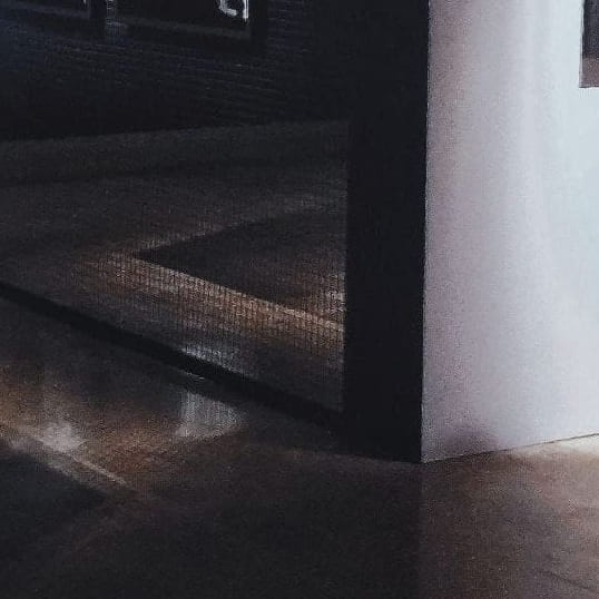 Cropped image of a dark exhibition space, focusing on triangular shapes formed by shadows on the floor.