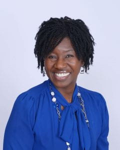 Portrait Kesha Morant Williams, smilling black woman in a royal blue shirt against a gray background