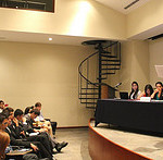 Debate stage with four students and a faculty facilitator in front of a large lecture style audience.