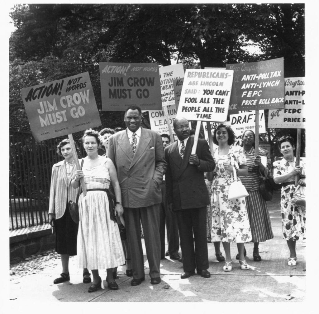 Paul Robeson stands in a crowd of demonstrators holding signs against Jim Crow
