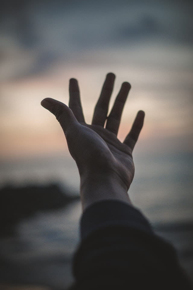 forearm and hand with palm facing the sky. The background is an out of focus sunset on a beach