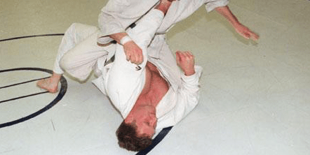 Kevid Szott in a wrestling pose. He is wearing an open karate gee and flipping his opponent onto their back.