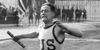 Larry Shields running relay. He has an intense look on his face and a relay bar in his hand. He is in the middle of a long stride while running.