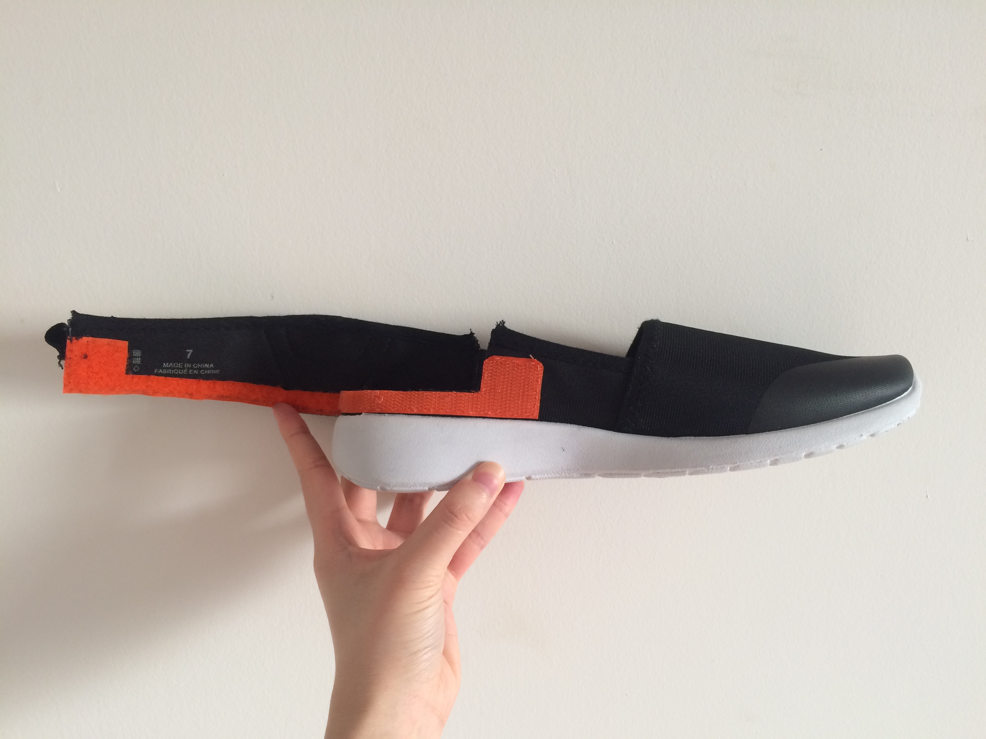 Peel Heel sample: a hand holds up a black shoe with orange velcro that allows the heel to be deattached